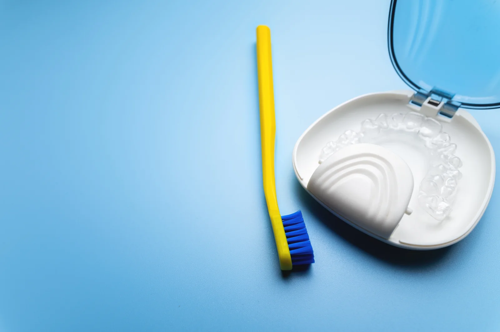 Transparent dental tray in an open storage case beside a toothbrush on a blue surface.